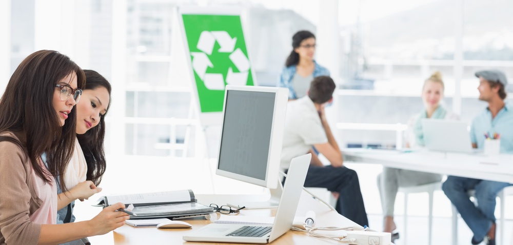 Casual group artists working at desks with recycling sign in background at a bright office